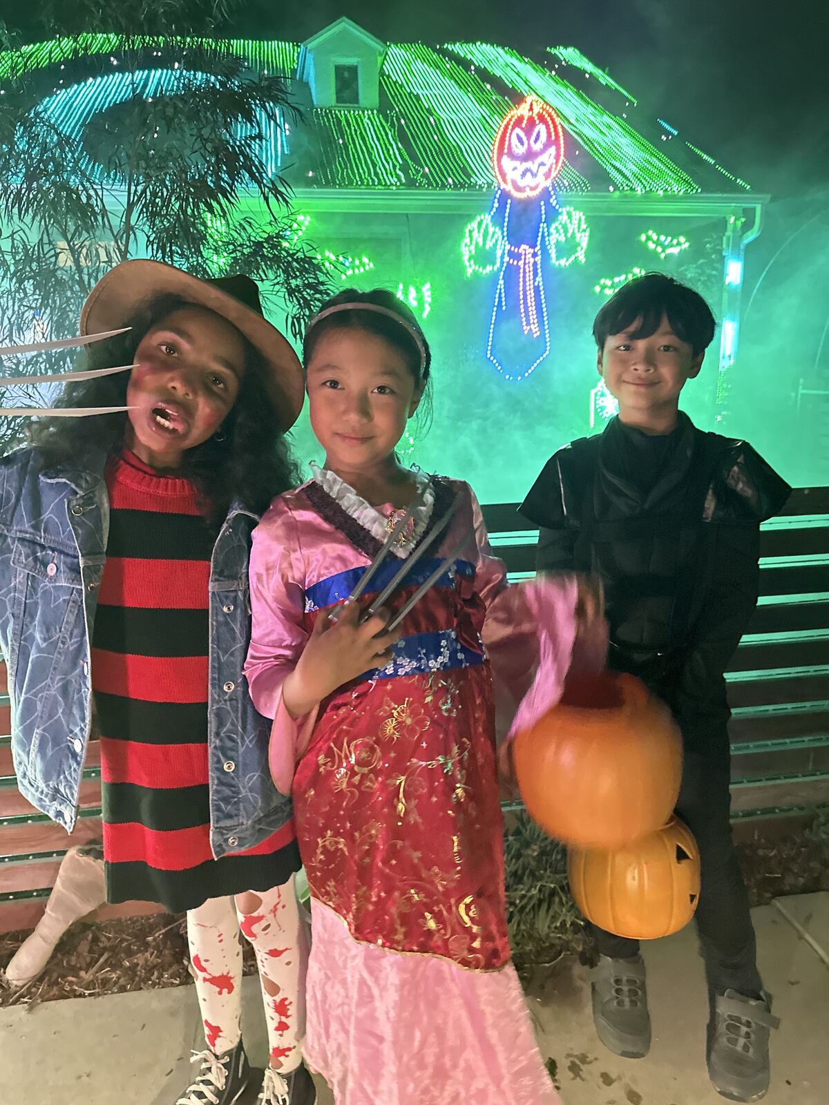 Children in Halloween costumes holding pumpkins in front of the glowing Lights on Falcon display